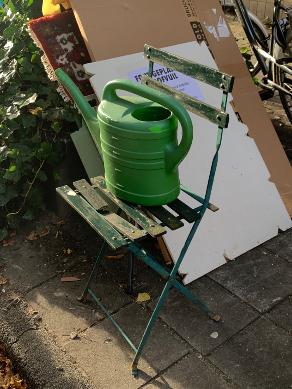 Green garden chair with one plank broken and a watering can